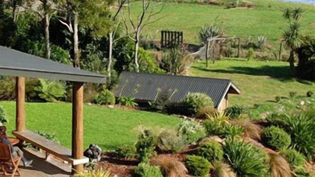 A patio area with a table and chairs, overlooking a grassy landscape with a pond and trees. - Beach Hideaway (Barrytown)