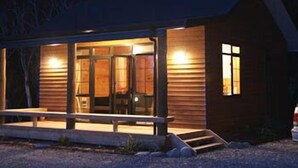 A wooden cabin with a porch, large windows, and a staircase leading to the entrance. - Beach Hideaway (Barrytown)