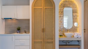 A modern bathroom with a large wooden door, a sink with a mirror above it, and a towel rack. - Romantica Apartments (Kithira)