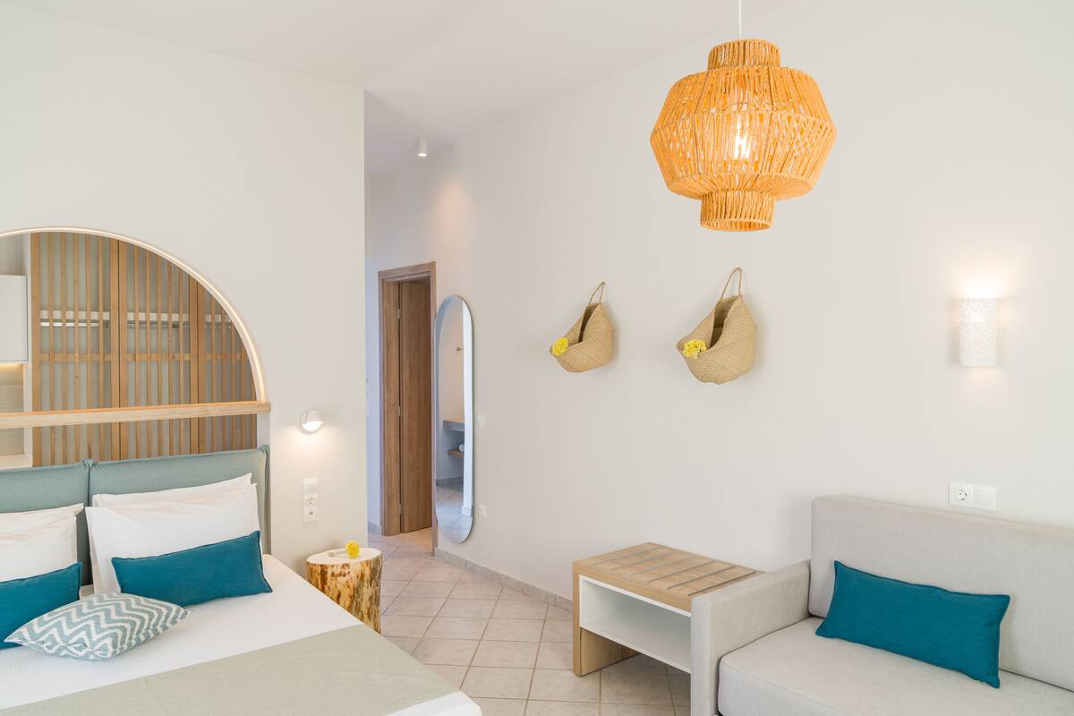 A modern bedroom with a bed, a sofa, a small table, and a hanging light fixture.