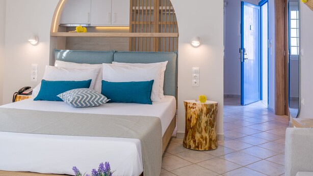 A modern bedroom with a bed, bedside tables, a small round table with a plant, and a hallway leading to another room. - Romantica Apartments (Kithira)