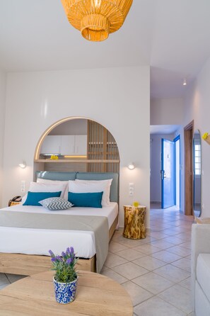 A modern bedroom with a bed, bedside tables, a small round table with a plant, and a hallway leading to another room. - Romantica Apartments (Kithira)