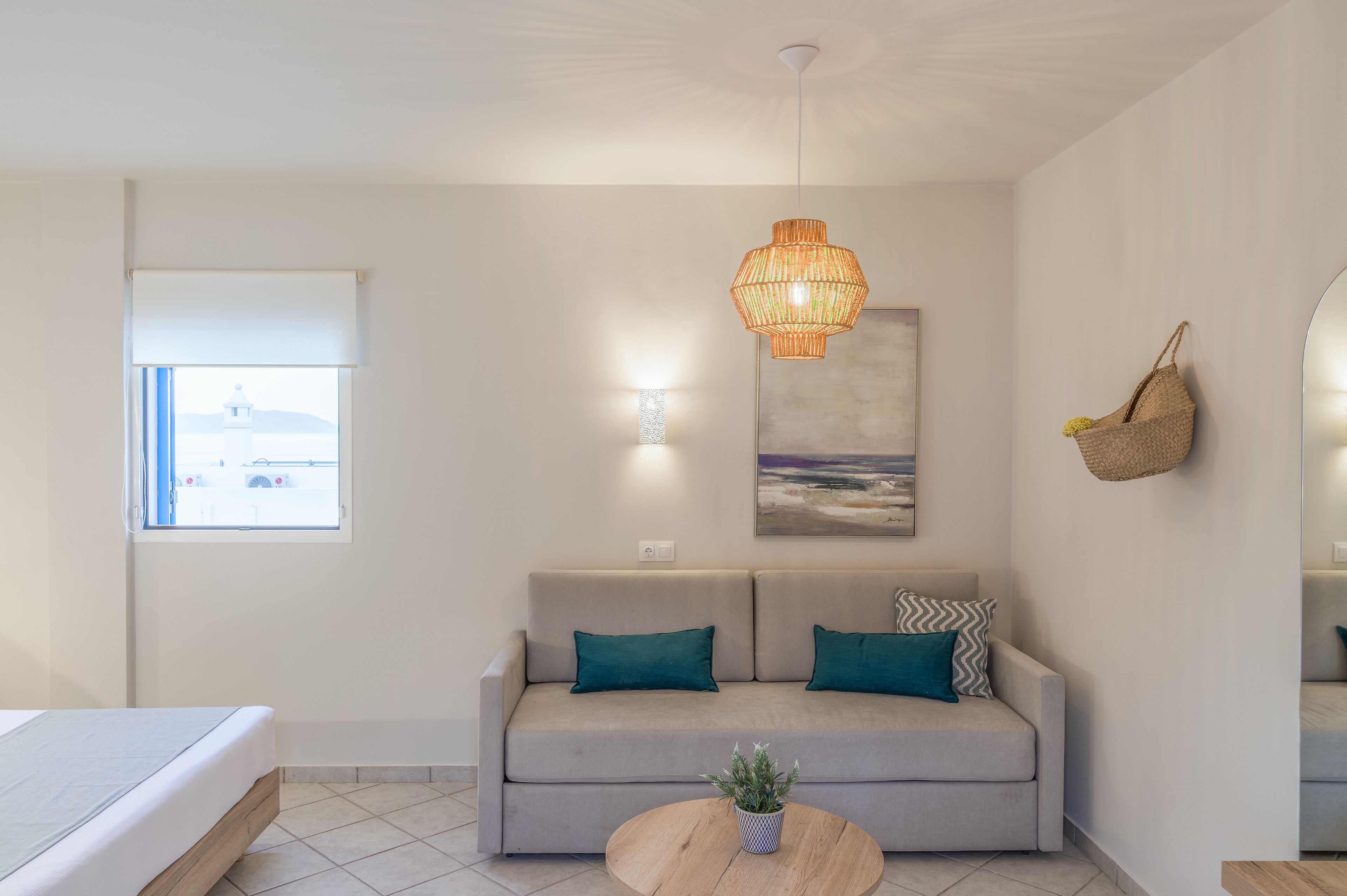 Una sala moderna con un sofá, una mesa redonda de centro con una planta, una cesta colgante de mimbre y un cuadro en la pared.