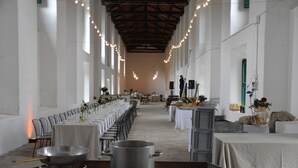 A long dining hall with tables set for a meal, a stage with speakers, and a person adjusting equipment. - Agriturismo Pantano Borghese (Rome)