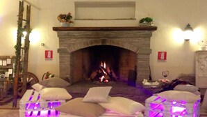 A cozy room with a stone fireplace, wooden pallets as seating, and a fire burning. - Agriturismo Pantano Borghese (Rome)