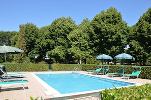 Una piscina con sillas de descanso y sombrillas, rodeada de vegetación.