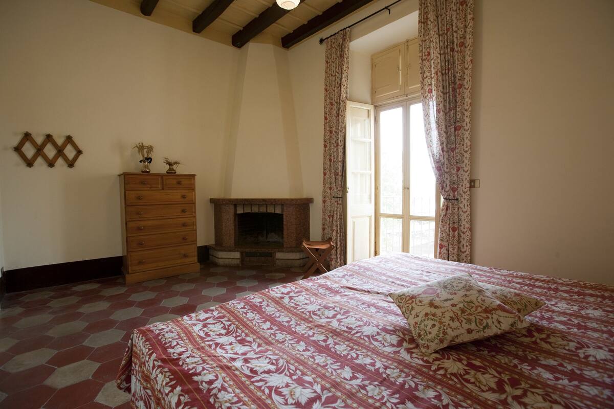 A bedroom with a bed, dresser, and fireplace.