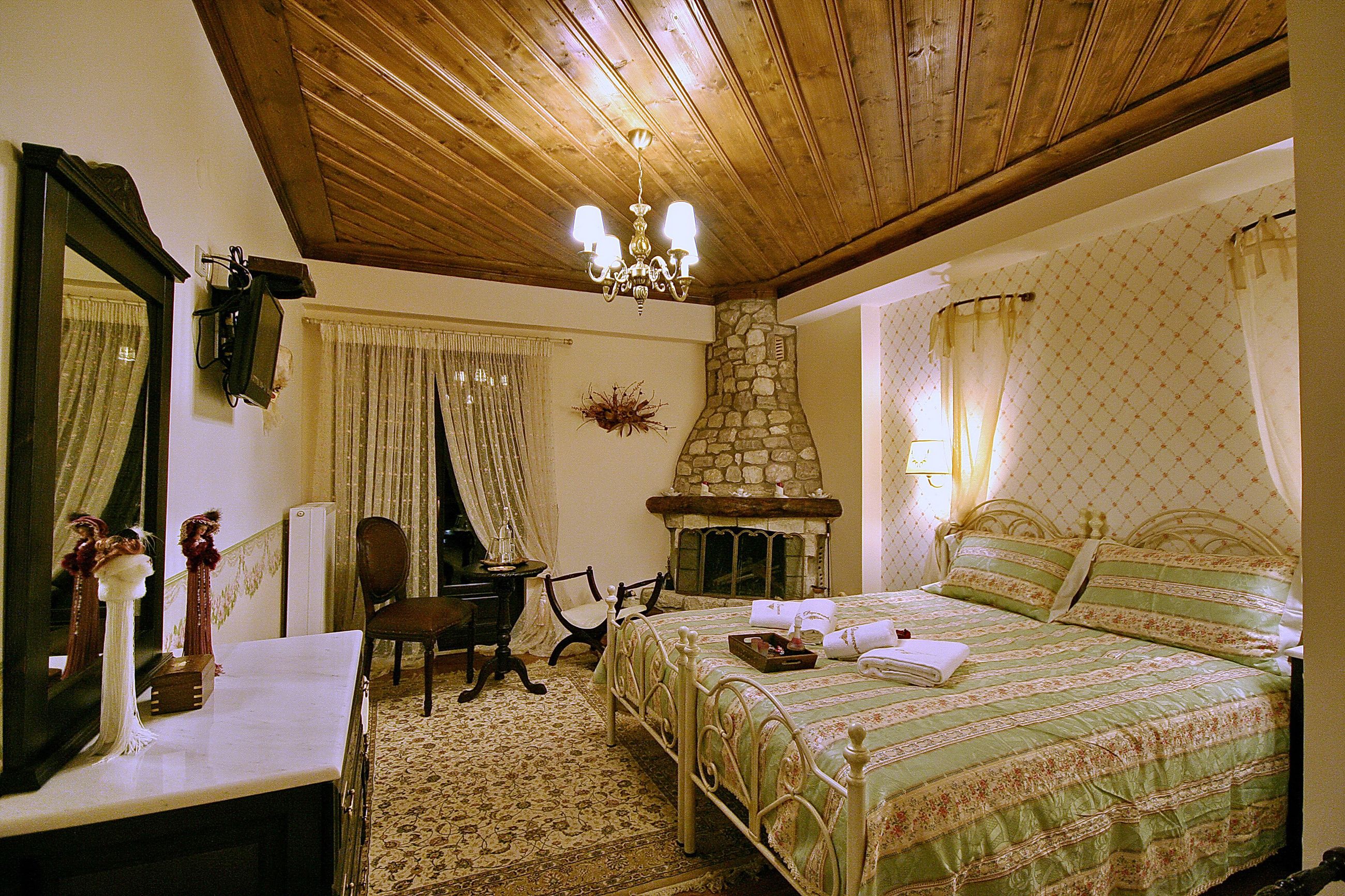 A bedroom with a stone fireplace, a bed with green bedding, a wooden ceiling, and a mirror on the wall.