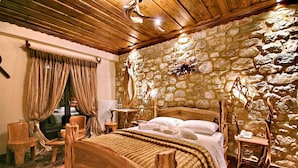 A rustic bedroom with a stone wall, wooden bed, and a small wooden side table.