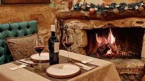 A cozy dining area with a fireplace, a table set for two, and a plush green armchair.