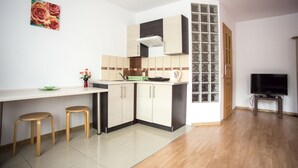 A compact kitchen with a white countertop, wooden stools, a coffee maker, and a television.