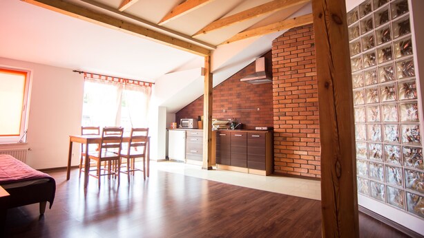 A spacious room with a wooden ceiling, a brick wall, and a kitchen area with cabinets and a microwave.