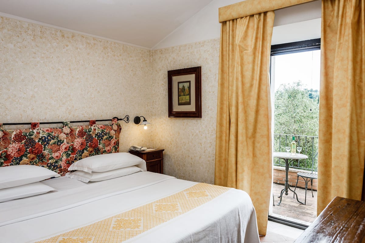 A hotel room with a bed, a nightstand, a framed picture, and a view of an outdoor balcony.