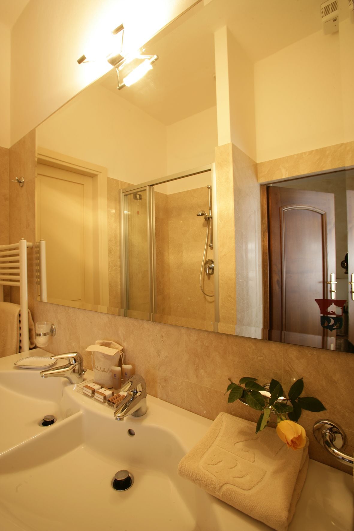 Une salle de bain avec un grand miroir, un lavabo, une douche et un porte-serviettes.