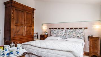 A bedroom with a large wooden wardrobe, a floral headboard, and a bedside table with a lamp.