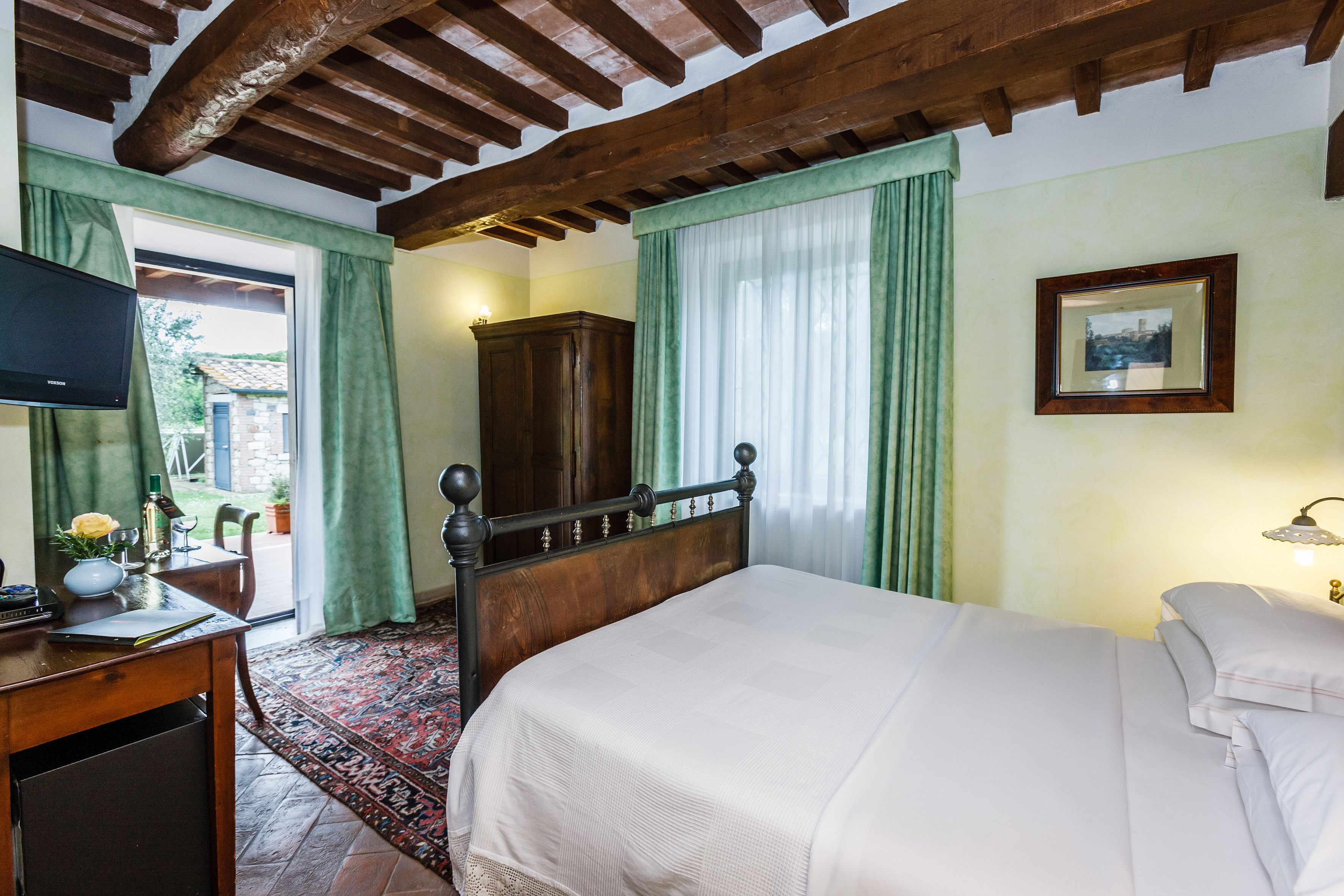 A bedroom with a wooden bed, a desk with a television, a wardrobe, and a window with curtains.