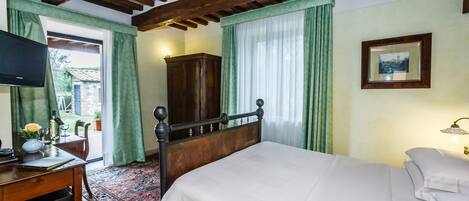 A bedroom with a wooden bed, a desk with a television, a wardrobe, and a window with curtains.