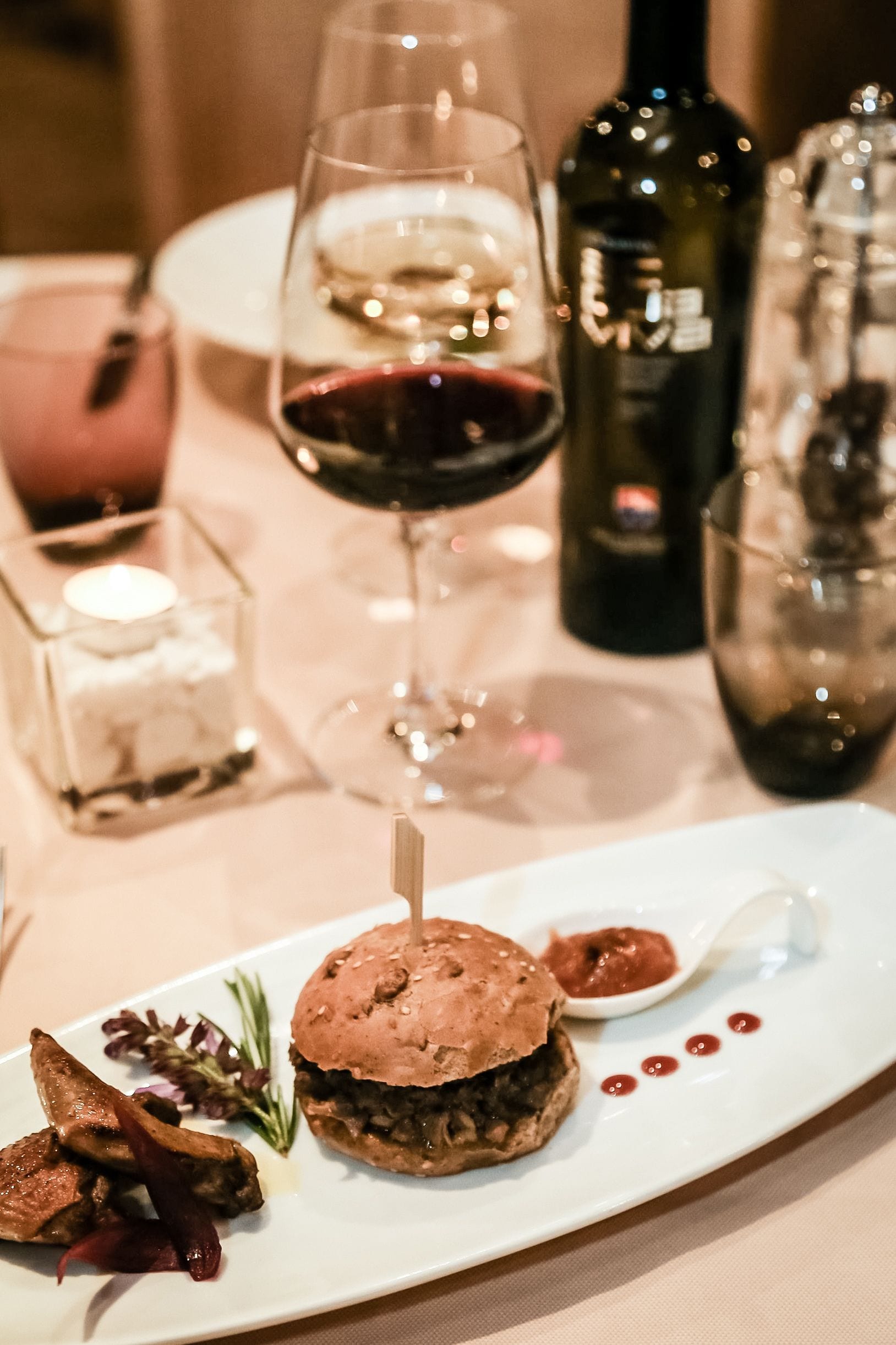 Una mesa de comedor con un plato de comida, una copa de vino y una botella.