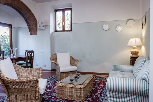 Una sala de estar con muebles de mimbre, un tapete estampado y un ventanal con vistas.