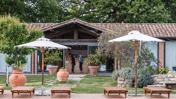 A pool area with lounge chairs and umbrellas, a building with a tiled roof, and a pathway leading to a door. - Villa Acquaviva Wine Resort (Manciano)