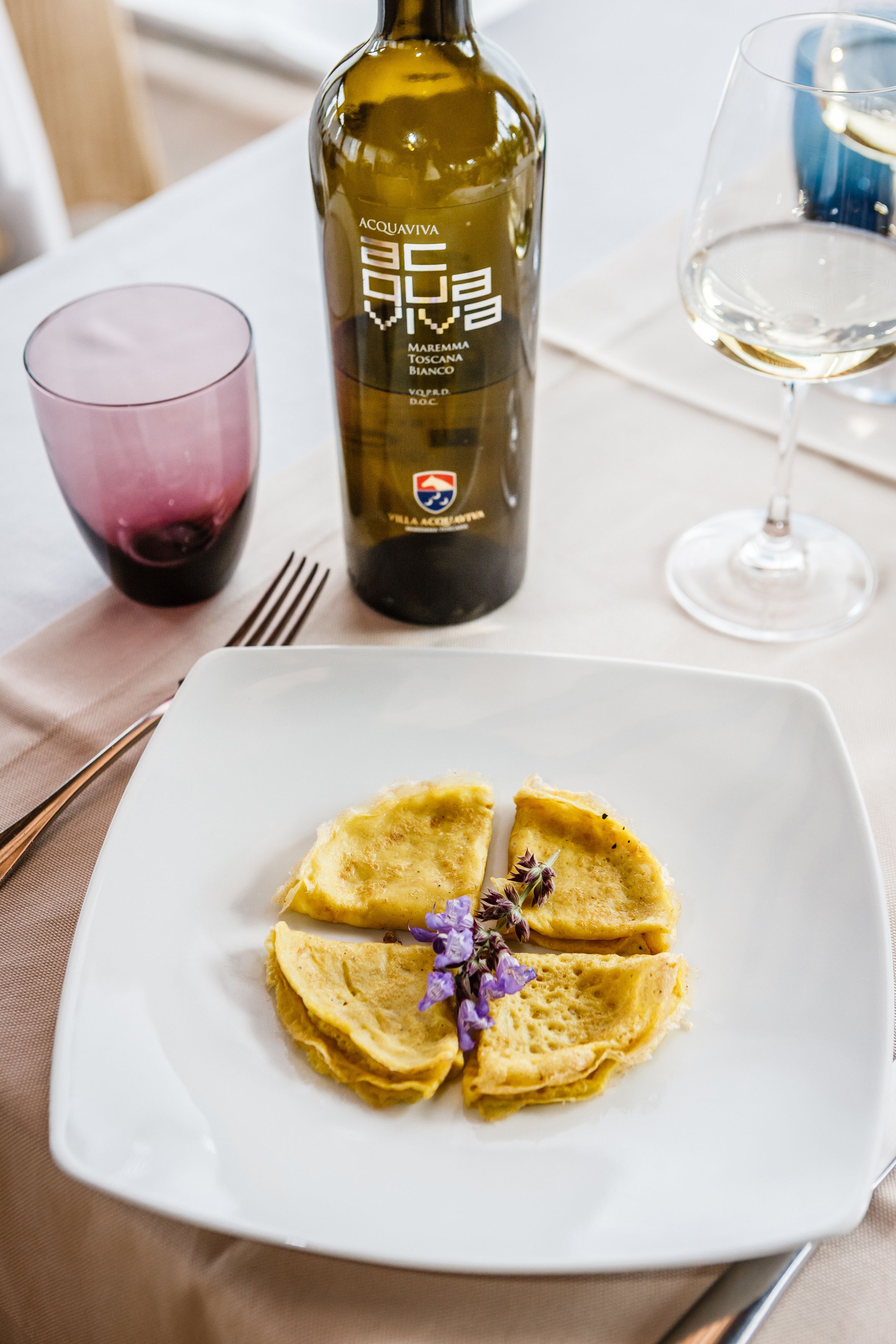 A plate with a folded dish, a bottle of wine, and two glasses on a table.