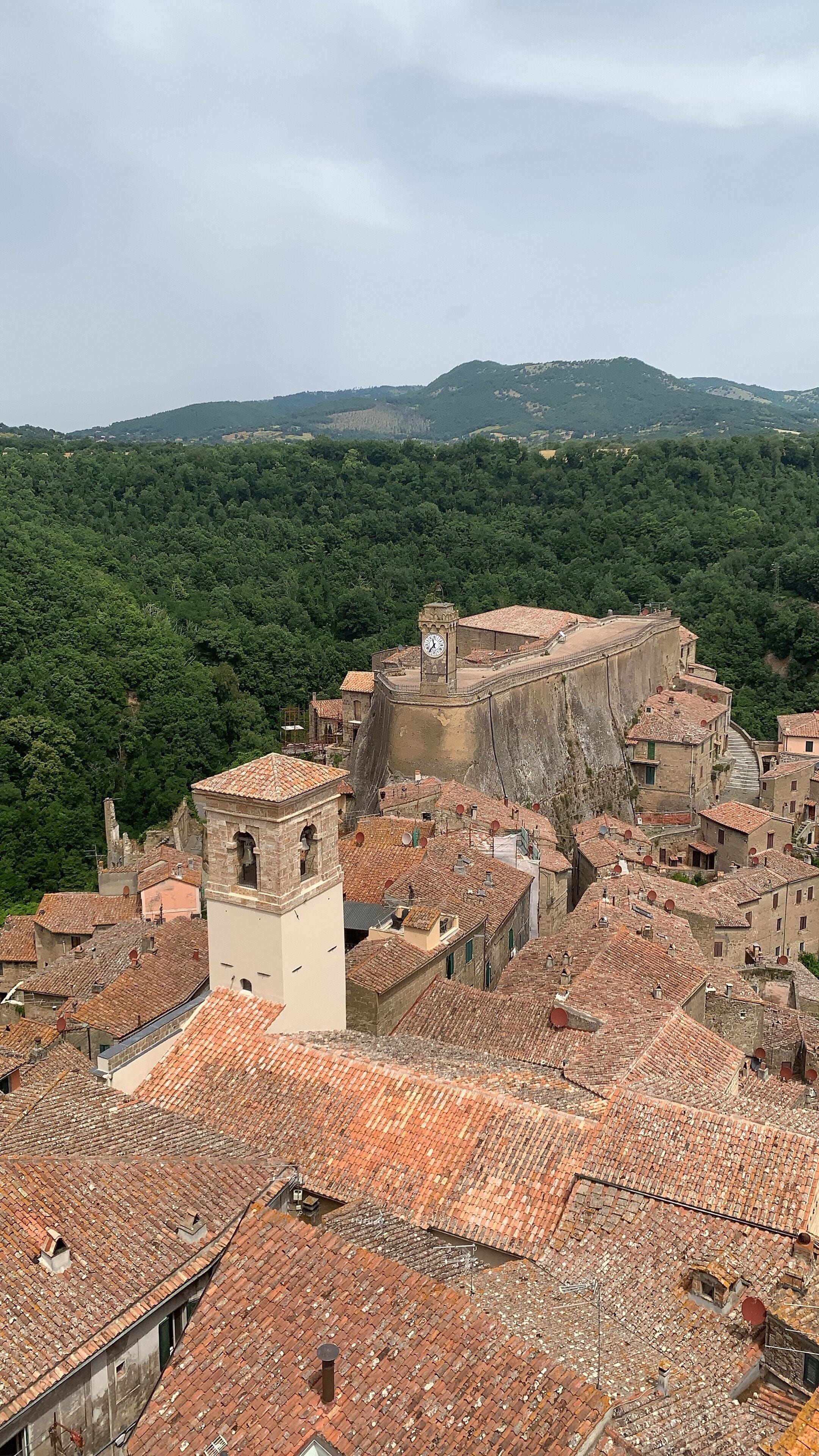 A historic town with a prominent stone fortress, terracotta-roofed buildings, and lush green hills in the background.