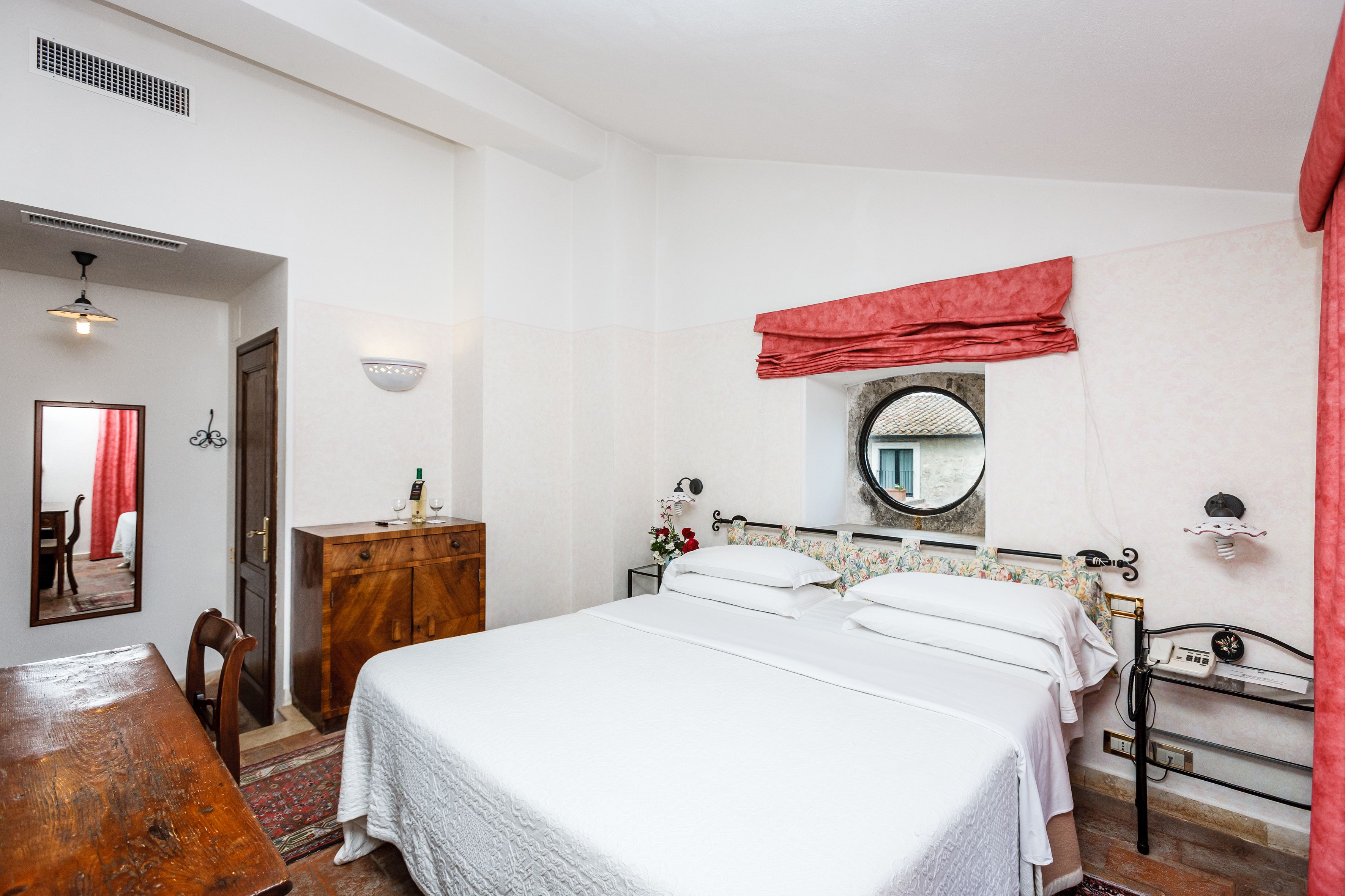 Une chambre à coucher avec un lit, une commode en bois, un miroir et un rideau rouge.