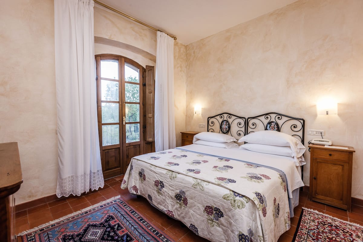 A bedroom with a bed, two bedside tables, a nightstand, a window with curtains, and a door.