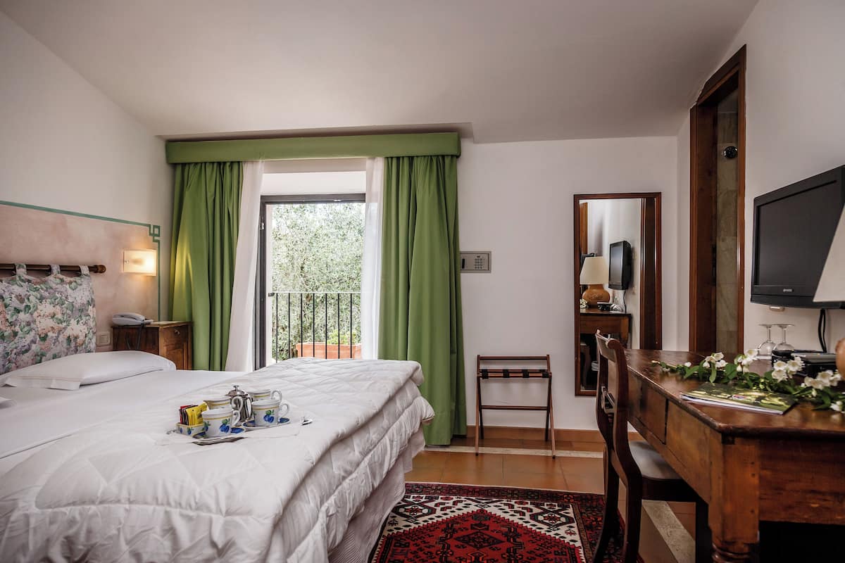 A hotel room with a bed, a desk, a chair, a television, and a window with green curtains.