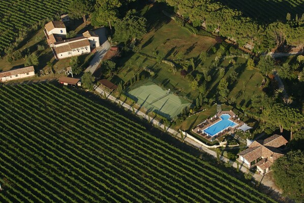 An aerial view of a property with a swimming pool, tennis court, and vineyard.