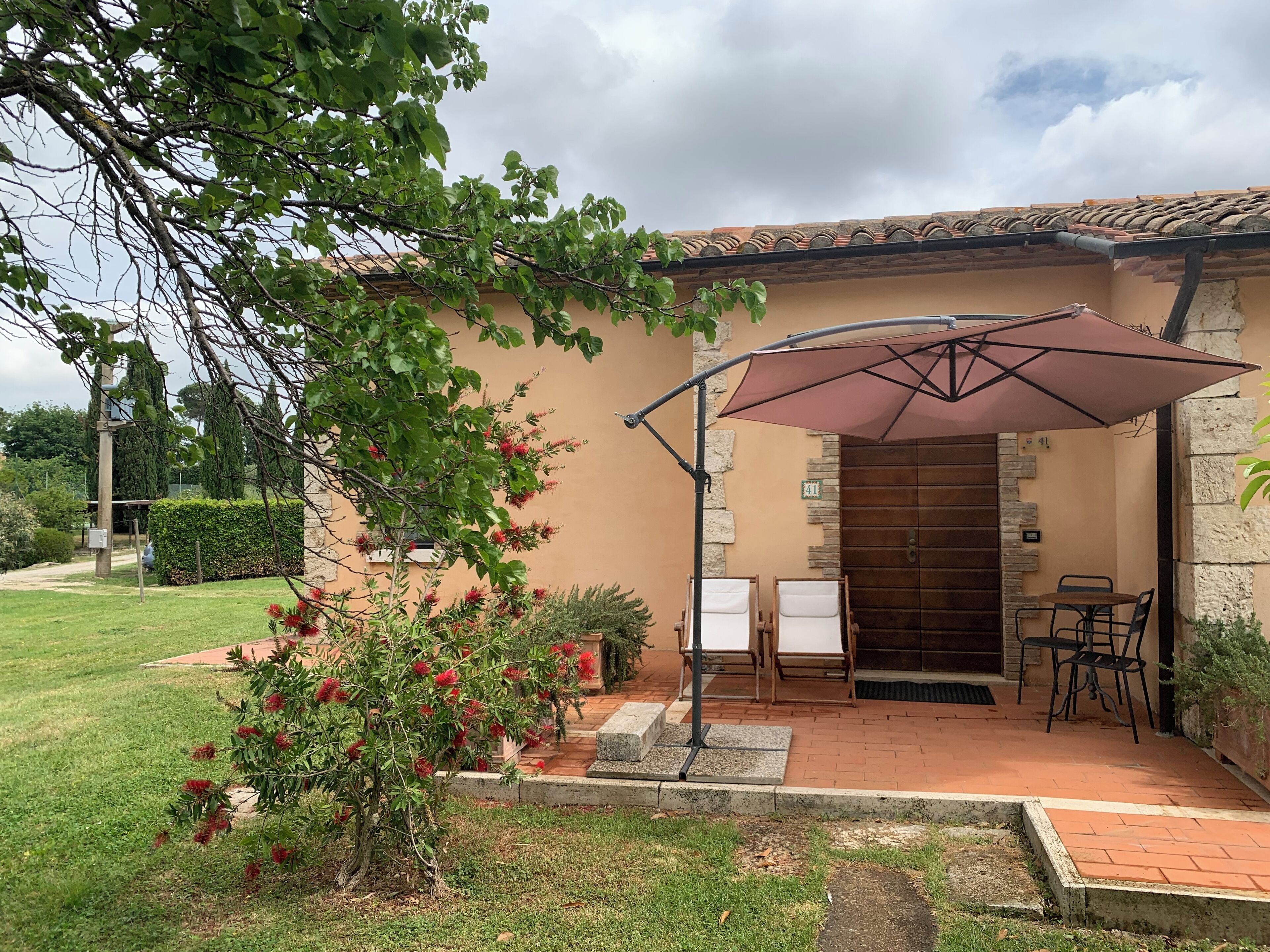Un patio con una mesa y sillas, un espacio de estar cubierto y una puerta que da a un edificio.