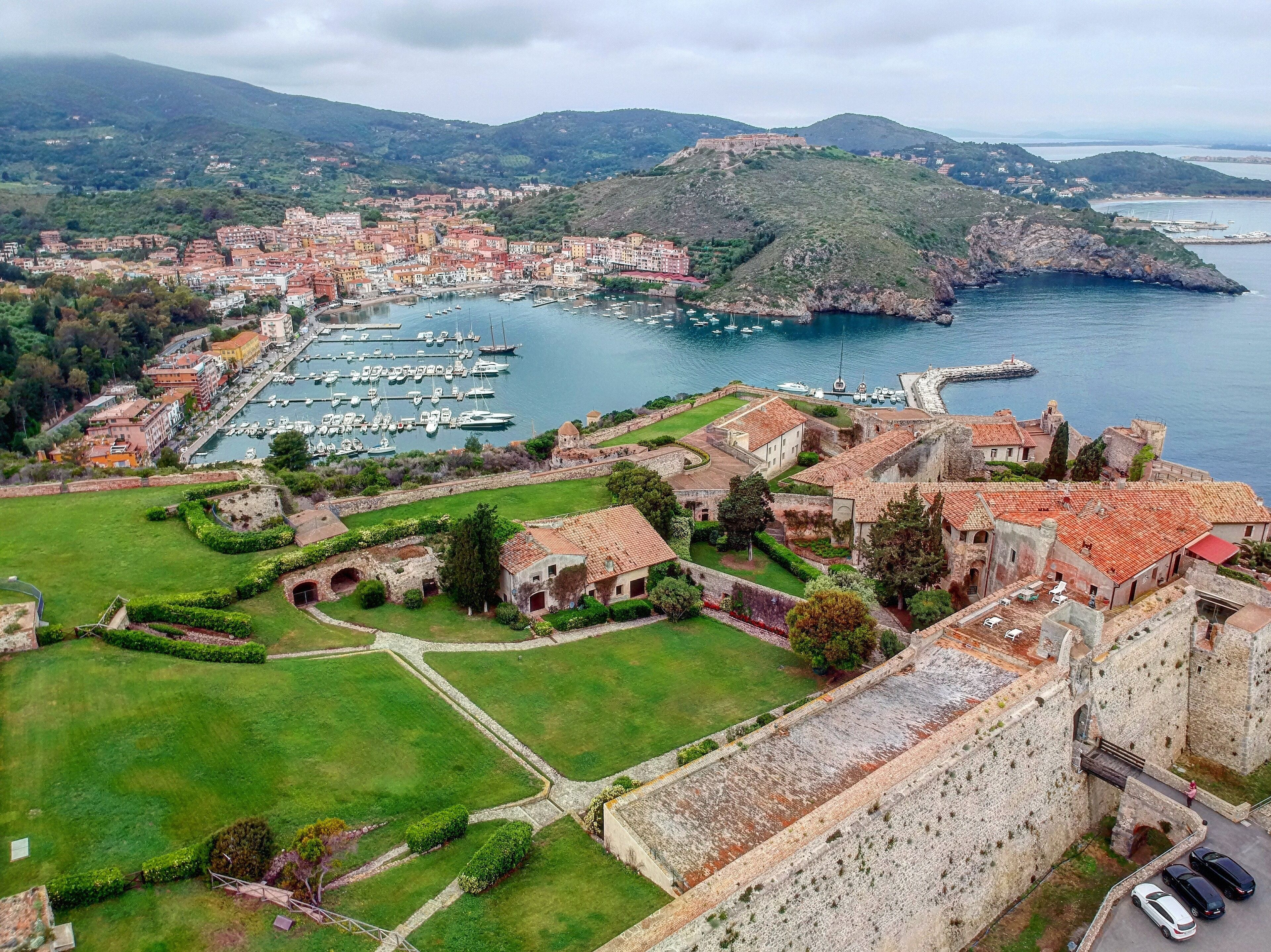An aerial view of a coastal town with a marina, historic buildings, and a fortified structure.