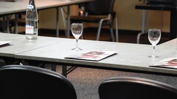 Un salón de conferencias con una mesa dispuesta para una reunión. Hay una botella de agua, dos copas de vino vacías y una revista sobre la mesa.