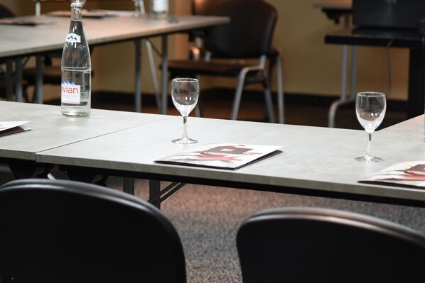 Un salón de conferencias con una mesa dispuesta para una reunión. Hay una botella de agua, dos copas de vino vacías y una revista sobre la mesa.