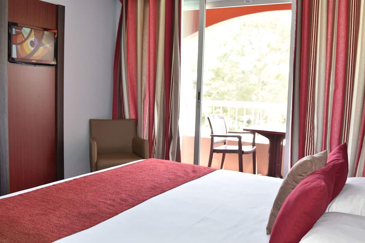 Una habitación de hotel con cama, una silla, una mesa y un balcón con cortinas.