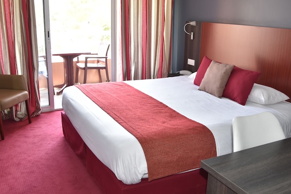 A hotel room with a large bed, a desk, a chair, and a view of the outdoors.