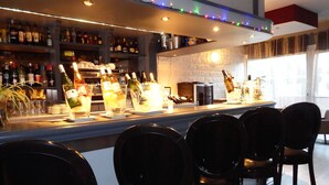 Un espace bar avec de nombreuses bouteilles d’alcool, des verres et un comptoir. On peut voir des chaises au premier plan.