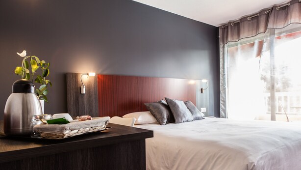 Une chambre d’hôtel moderne avec un grand lit, une table de chevet avec une lampe et une vue sur l’extérieur par une fenêtre.