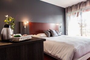 Una habitación de hotel moderna con una cama grande, una mesita de noche con lámpara y vistas al exterior a través de una ventana.