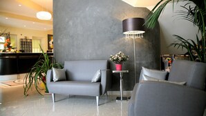 Un hall d’entrée moderne avec un canapé gris, une lampe sur pied et une plante en pot.