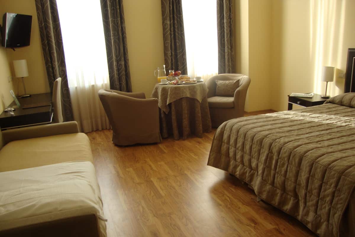 Hotelkamer met een bed, twee stoelen, een klein tafeltje met ontbijtartikelen en een televisie aan de muur.