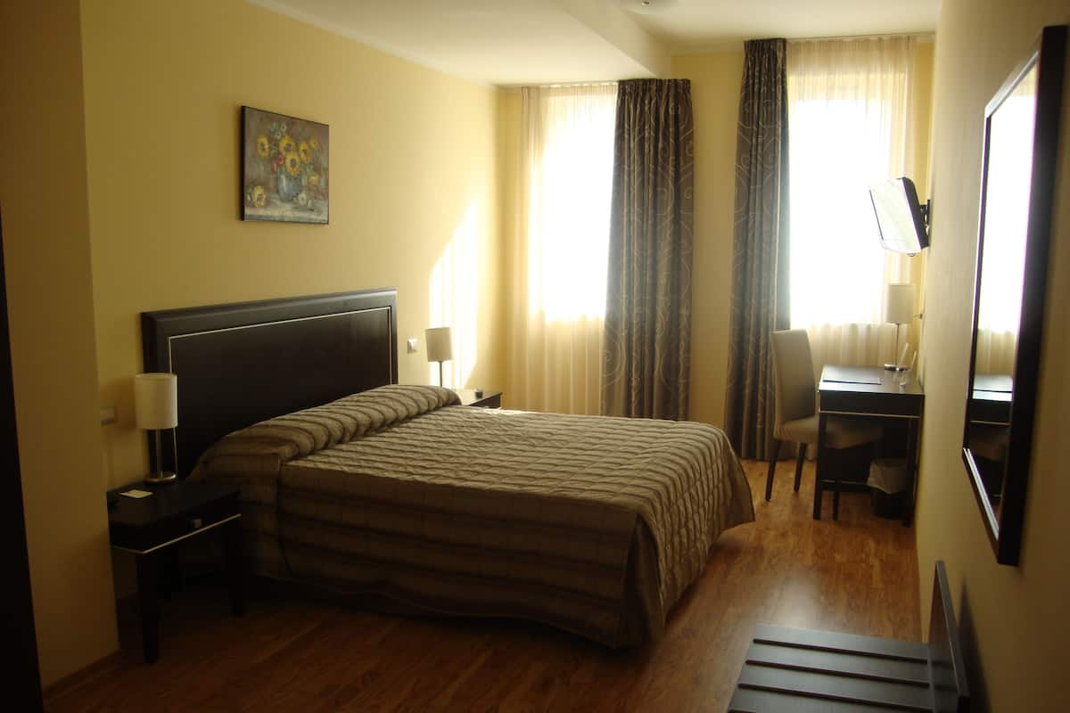 Een hotelkamer met een groot bed, een bureau met stoel, een lamp en een schilderij aan de muur.