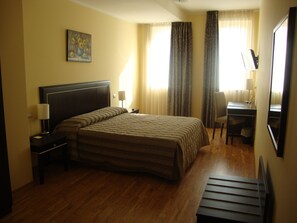 Quarto de hotel com uma cama grande, uma mesa com cadeira, uma luminária e um quadro na parede.