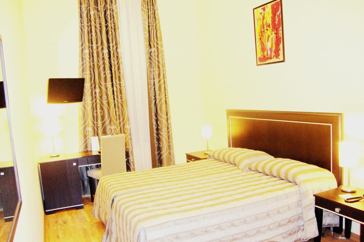 Een hotelkamer met een groot bed, een bureau, een stoel, een televisie en gordijnen.