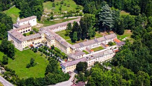 Une vue aérienne d’un vaste ensemble de bâtiments historiques, composé de plusieurs ailes et de cours intérieures, le tout entouré d’une végétation luxuriante.