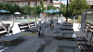 Une table dressée pour un repas en plein air, avec de la vaisselle transparente et des serviettes, entourée de chaises et de parasols.