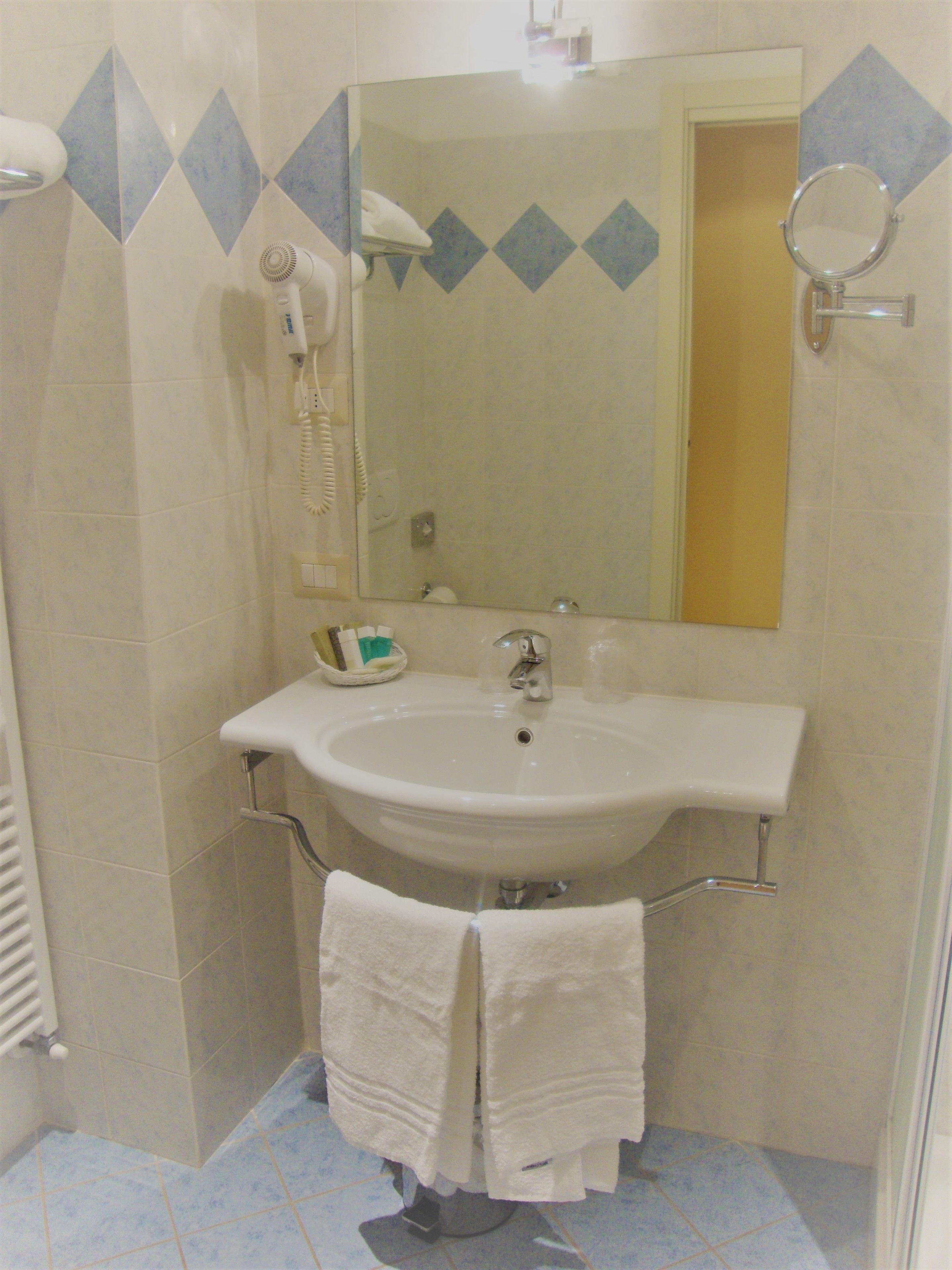 A bathroom with a sink, mirror, and a hairdryer mounted on the wall.