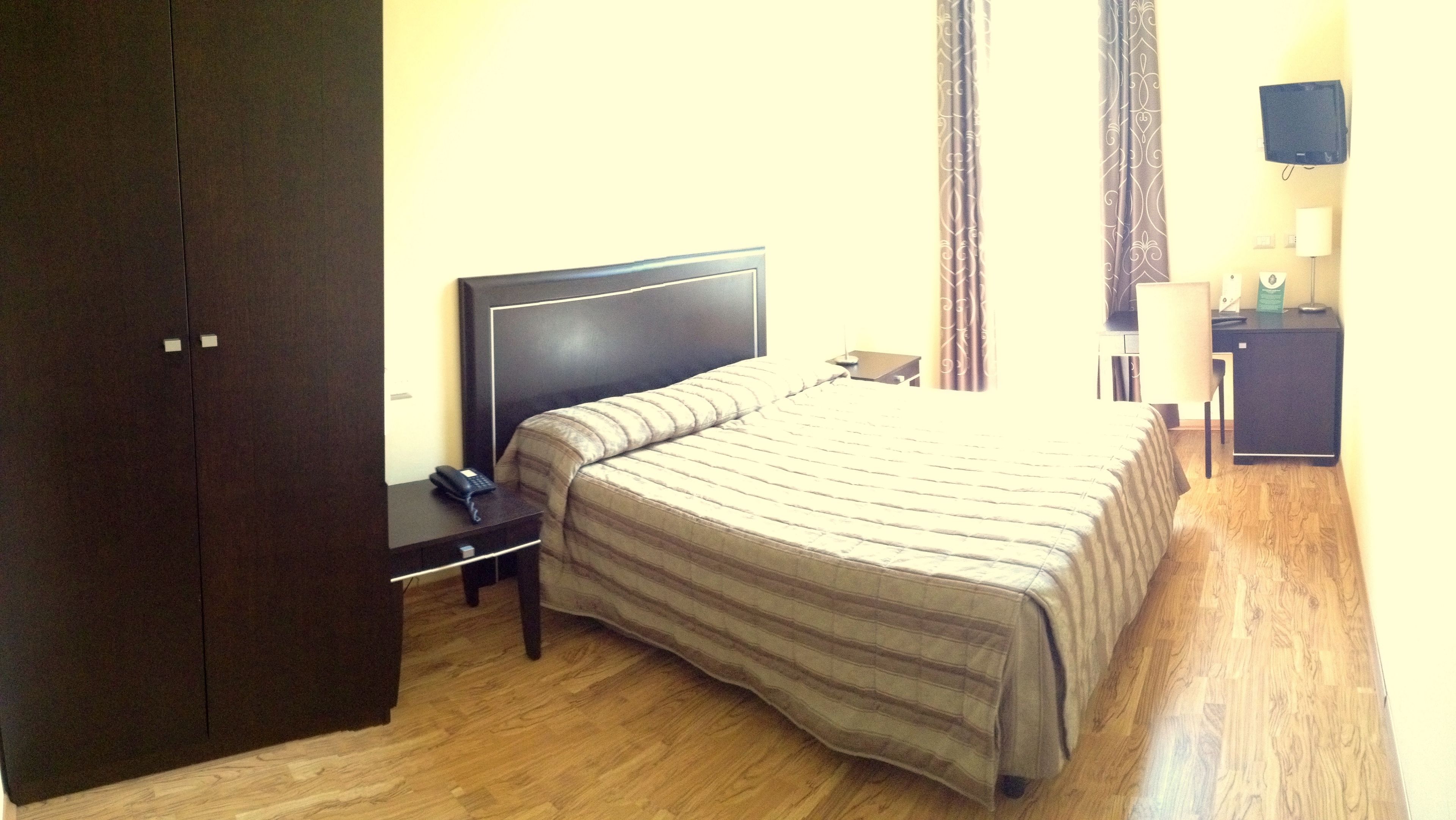 A hotel room with a bed, a desk, a telephone, and a TV.