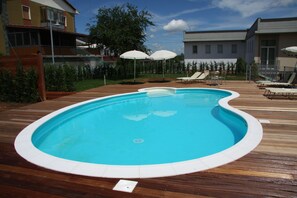 Piscina com deck de madeira, rodeada por espreguiçadeiras e guarda-sóis.