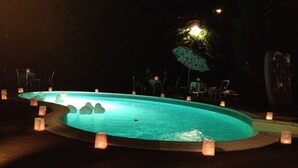 Une piscine dotée d’une terrasse en bois, entourée de bougies et agrémentée d’un parasol décoratif.